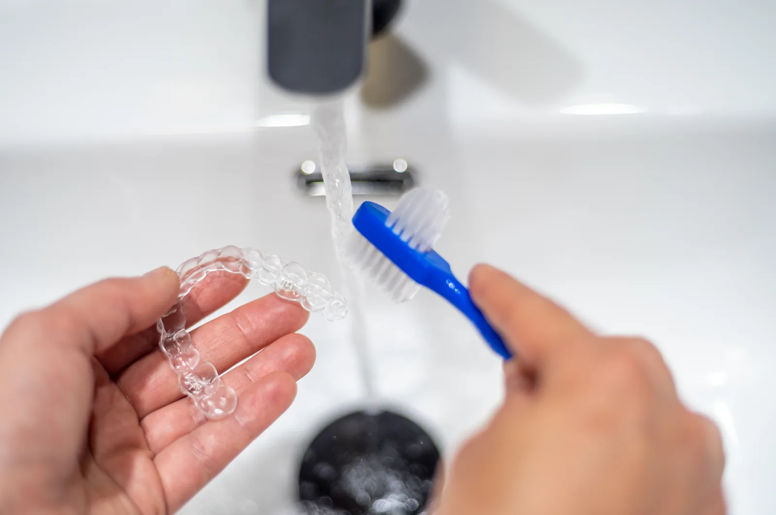 A woman cleaning an Invisalign aligner with a brush.
